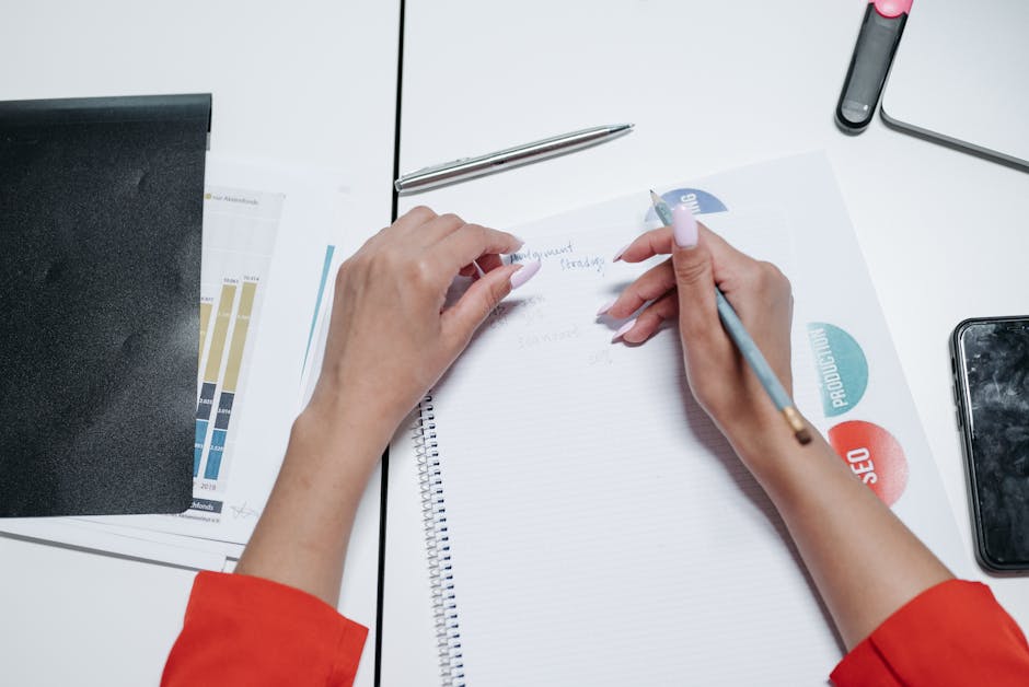 Close-up view of hands writing on a notepad with printed charts and graphs.